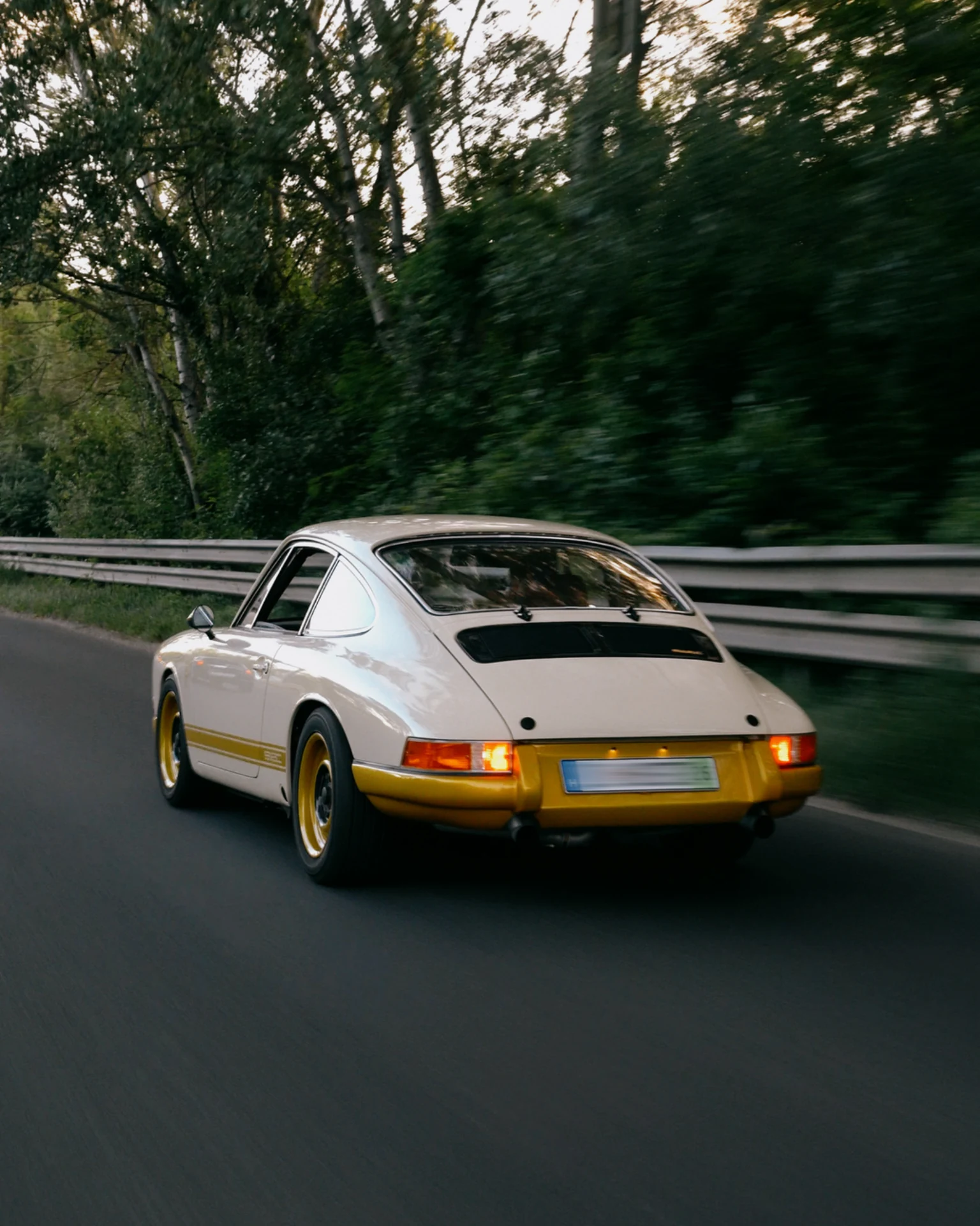 A silver and yellow KAMM 912 driving along a wooded road